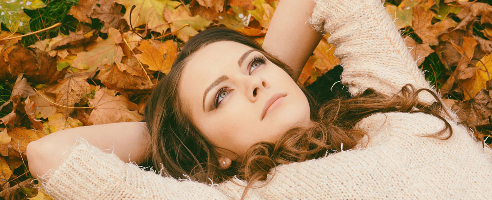 Girl lying in autumn leaves with her hands behind her head